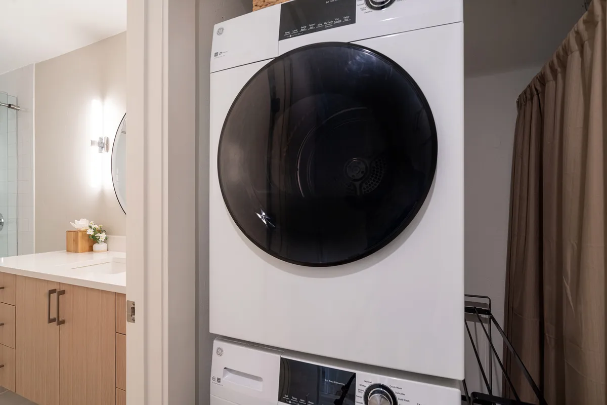 A well-organized laundry area features both a washing machine and a dryer, along with a vanity counter, all set within a bright and functional space. The area is tidy and designed for easy access to laundry essentials, making it convenient for guests staying extended periods.