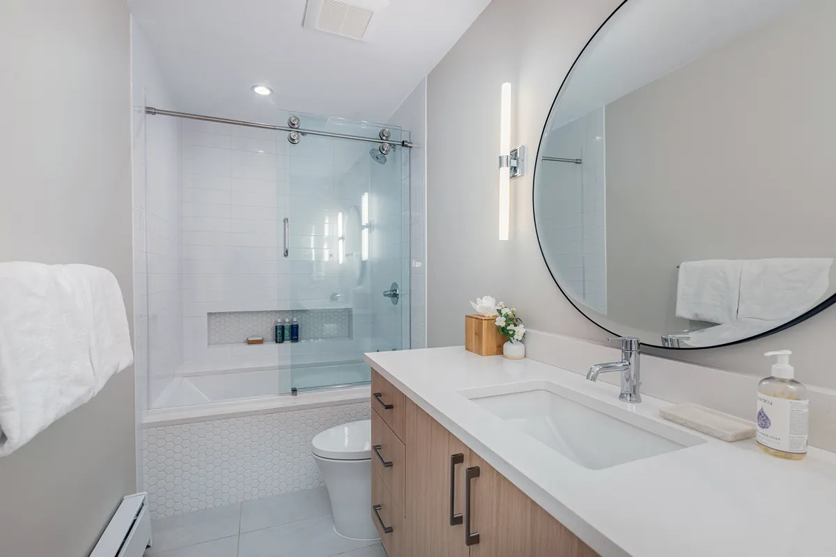 A modern bathroom featuring a large round mirror, sleek sink, and a glass-enclosed shower. The style is serene and inviting, promising a luxurious bathing experience and private relaxation.