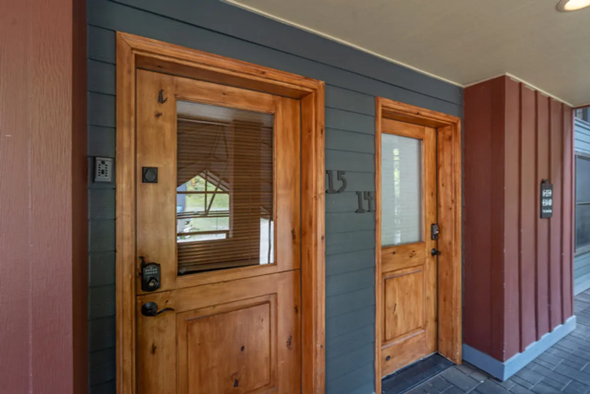 The main entryway showcases inviting wooden doors with numbered plaques against a textured wall, creating a welcoming first impression. The entry exudes warmth and a sense of arrival, suggesting both security and the comfort of a home-like environment.