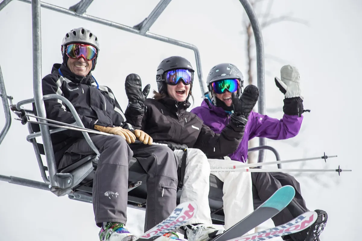 A dynamic winter scene featuring a ski lift in operation, several skiers gearing up for a run, and a snowy landscape that radiates the excitement of a day on the slopes. The environment is bustling with winter sports enthusiasts, hinting at direct access to skiing and the active atmosphere at the base of the mountain.