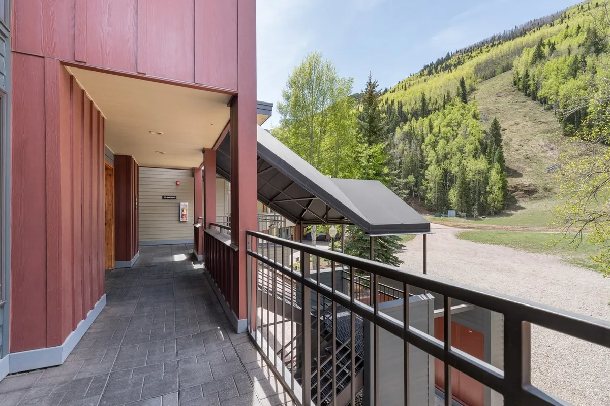 A tranquil view from a balcony at Cimarron Lodge, overlooking lush trees and the dramatic mountain landscape. The setting offers a peaceful retreat after an active day, emphasizing relaxation and the striking natural surroundings guests can enjoy from their accommodations.