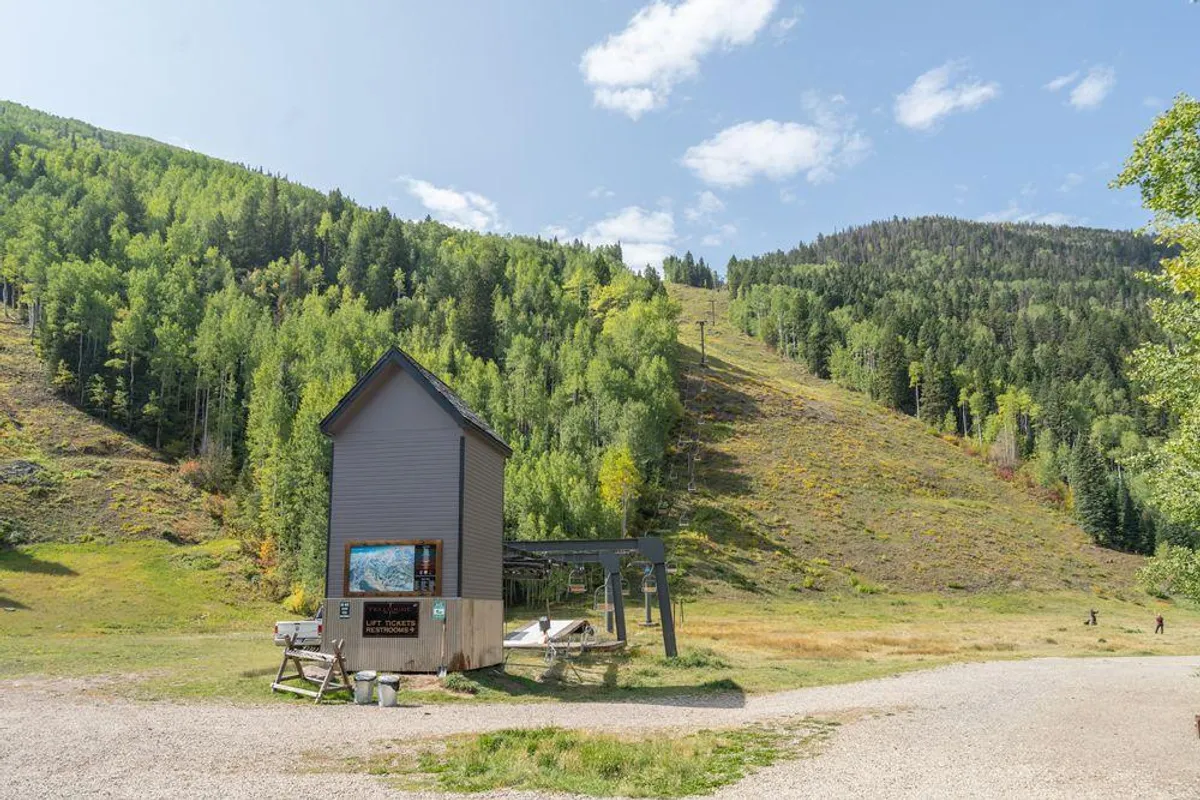 A crisp exterior shot showing a ski lift at the base of the slopes, with a small building and surrounding trees. The lift is right outside the lodging, visually reinforcing immediate ski access.